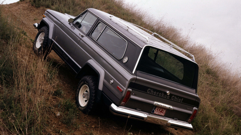 Gray 1978 Jeep Cherokee Chief SUV seen from left rear climbing a steep hill trail