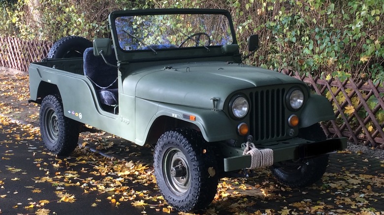 Green Jeep CJ-6 SUV front right view seen parked by a fence