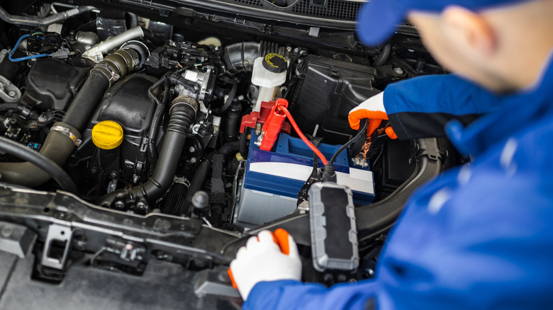 A mechanic using a portable jump starter to recharge a car
