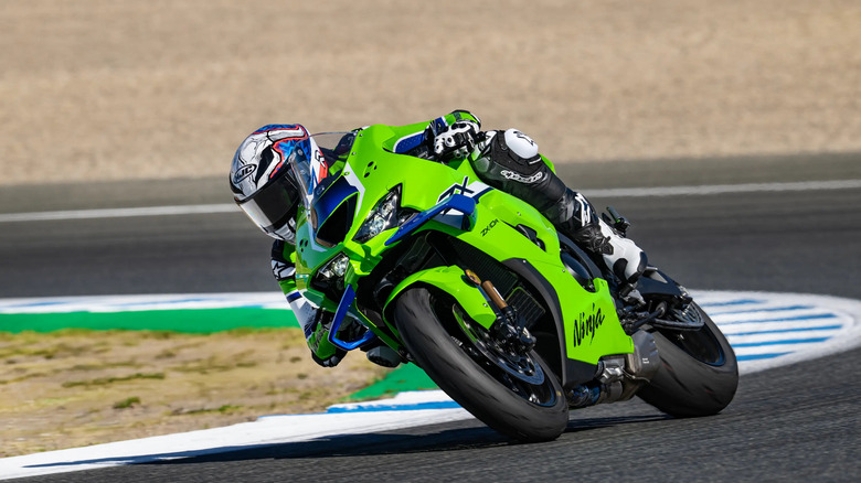 A lime green Kawasaki Ninja ZX-10R superbike leaning aggressively through a racetrack corner with a helmeted rider
