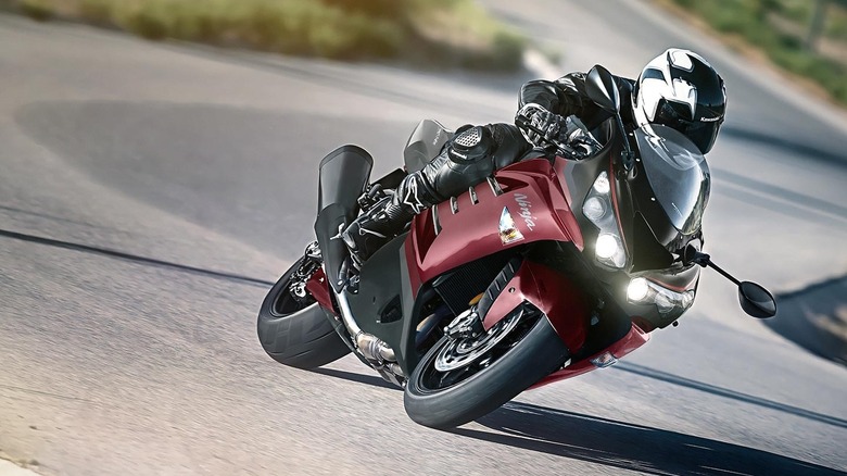 A dark red Kawasaki Ninja ZX-14R hyperbike leaning through a paved road bend with illuminated quad headlights.