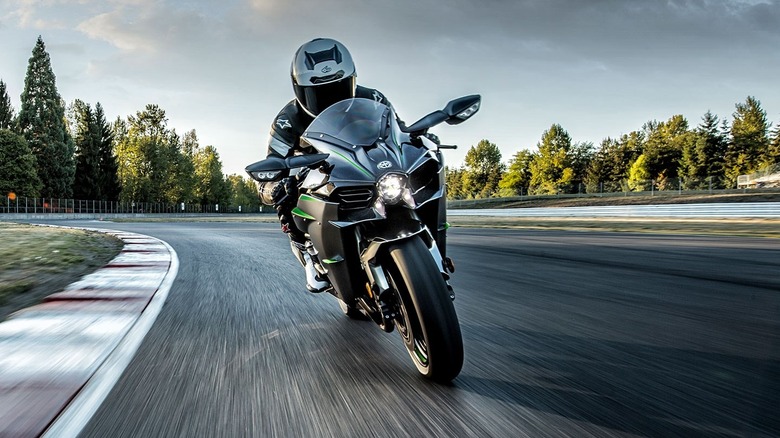 A rider wearing black leathers leaning a dark Kawasaki Ninja H2 superbike through a paved racetrack corner.