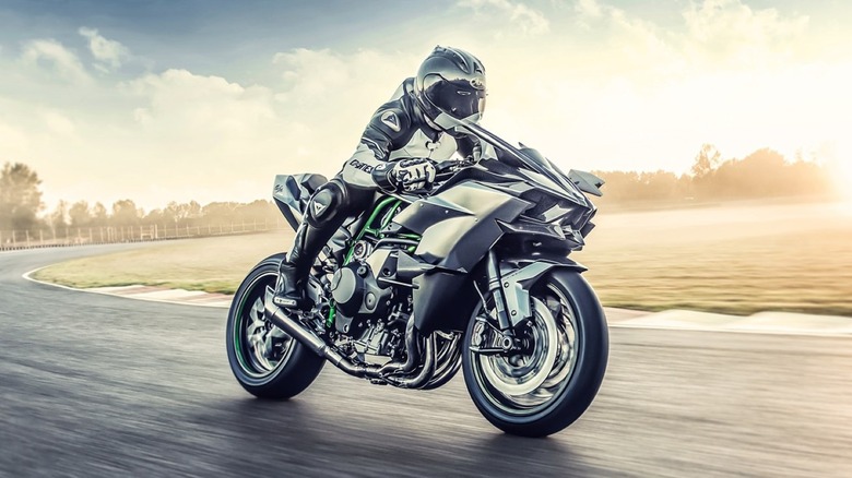 A track-only carbon fiber Kawasaki Ninja H2R motorcycle leaning through a racetrack curve at speed during golden hour.
