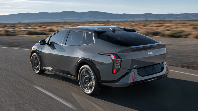 Rear 3/4 view of a grey Kia EV4 sedan driving on a desert road