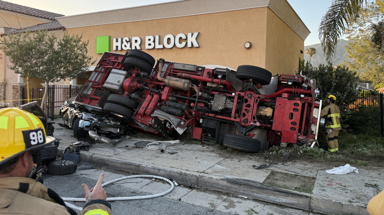 A photo of the underside of the flipped fire truck propped up against an H&R Block with firefighters in the picture