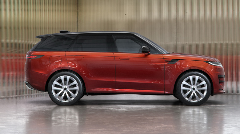 Side view of a red Range Rover Sport parked on a shuny surface in front of reflective corrugated walls