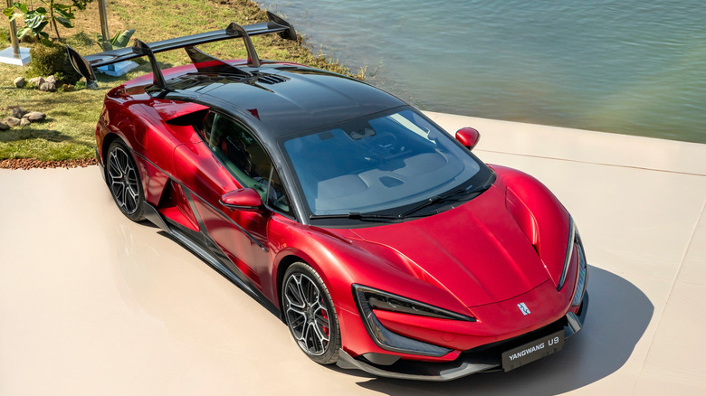A red YANGWANG U9 hypercar parked outside near water.