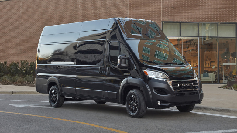 Front 3/4 view of a blacked out 2025 Ram ProMaster on a road with a brick building in the background