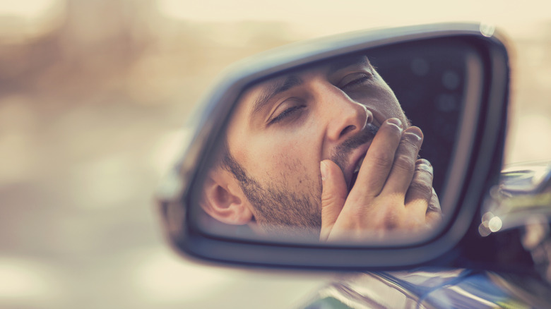 A reflection on a vehicle's side mirror of a driver yawning