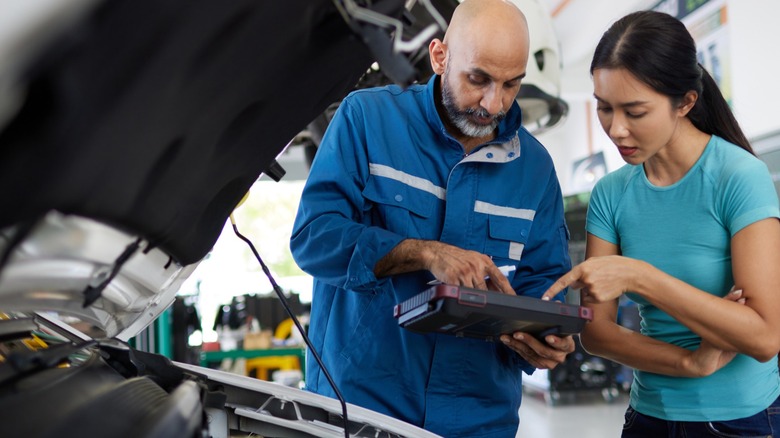 Mechanic speaking with customer next to raised hood of car