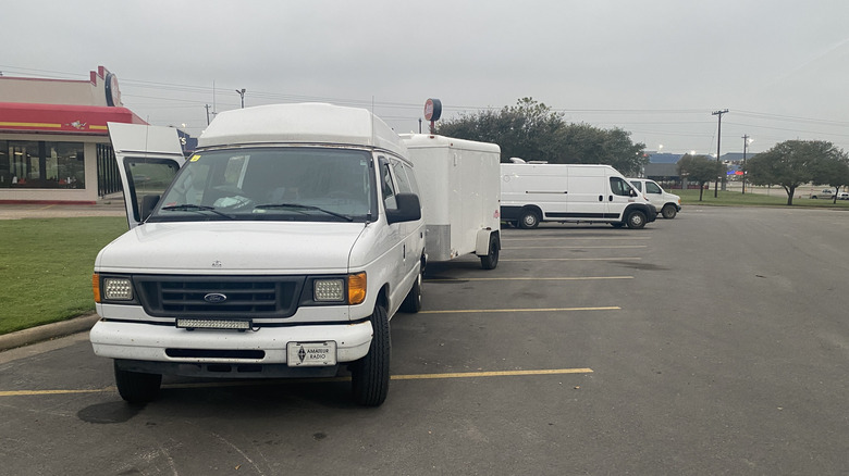 Various camper vans at the edge of a parking lot in a commercial area under a grey sky