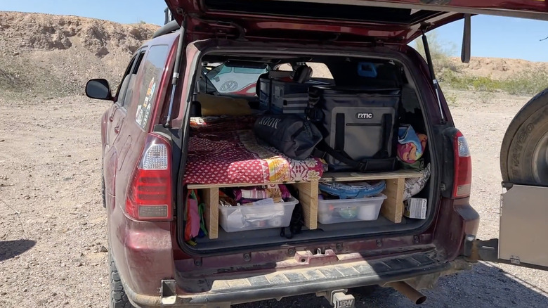 Rear view of a Toyota 4Runner with the hatch open, revealing a tiny home on wheels setup inside