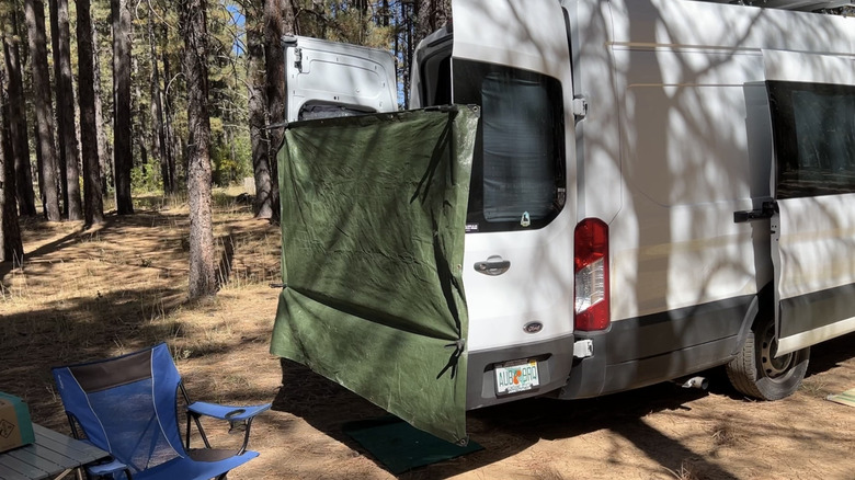Rear 3/4 view of a Ford Transit camper van with the back doors open and a tarp across them