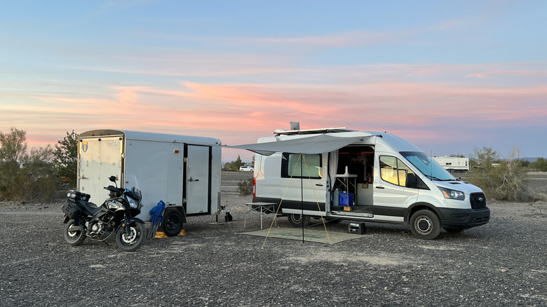 The author's van camp at sunset in the desert, including a cargo trailer, motorcycle, and Starlink