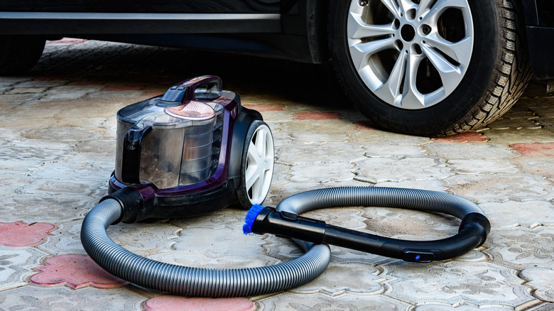 A vacuum cleaner on the driveway next to a car