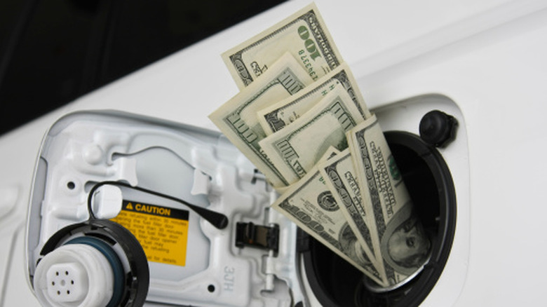 A bunch of $100 bills stuffed into the fuel filler of a car where the gas cap would normally be.