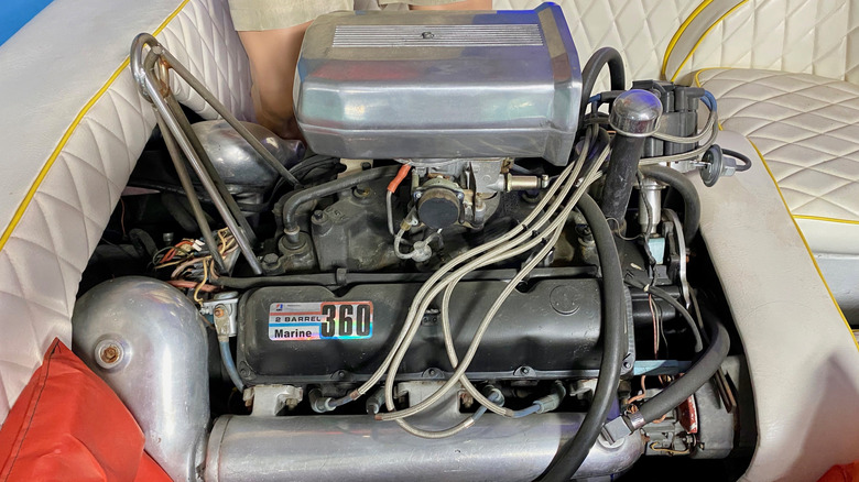 An AMC 360 V8 marine engine with a two-barrel carburetor and air scoop next to padded white seats in a boat