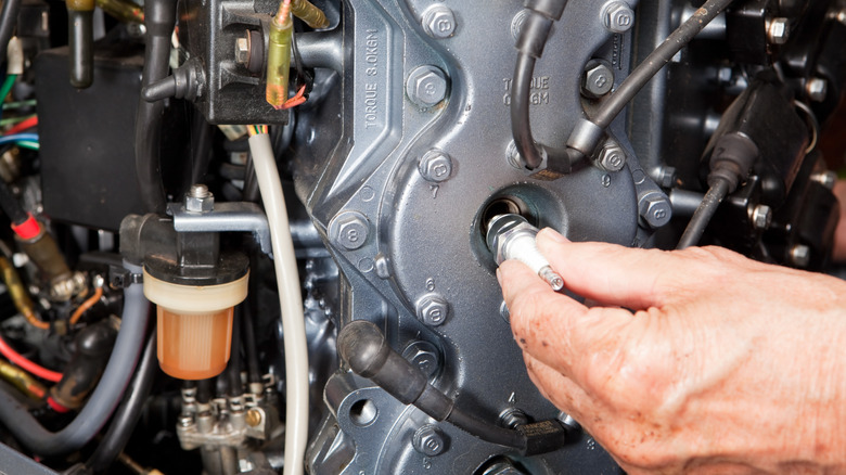 Removing a spark plug from a boat engine, surrounded by the engine's various ancillaries.