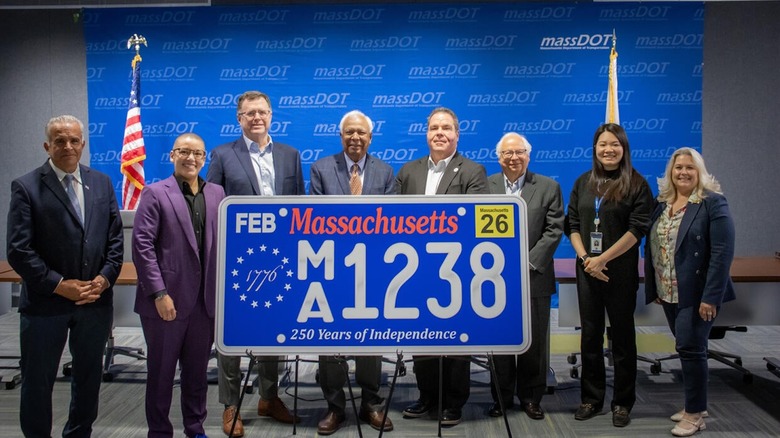 Massachusetts Registry of Motor Vehicles pose with a replica of the "250 Years of Independence" commemorative license plate