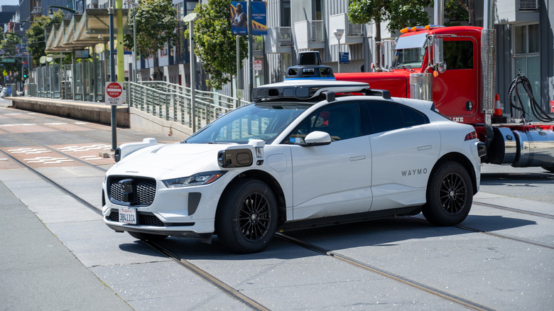 Autonomous Waymo Jaguar I-PACE self-driving car crossing light rail tracks in an urban street environment on a sunny day, San Francisco, California, April 28, 2026.