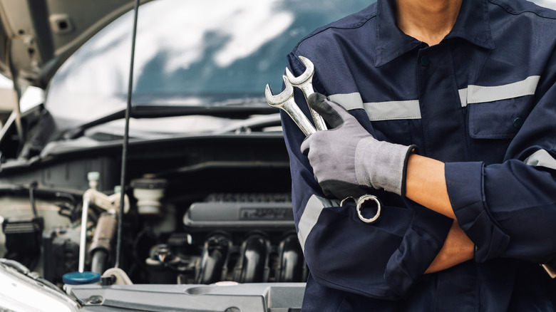 A mechanic holding wrenches in front of a vehicle in a service shop