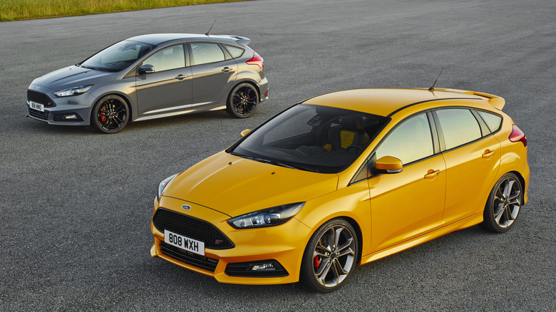 Two Ford Focus ST cars parked on a paved surface with grass field in the background