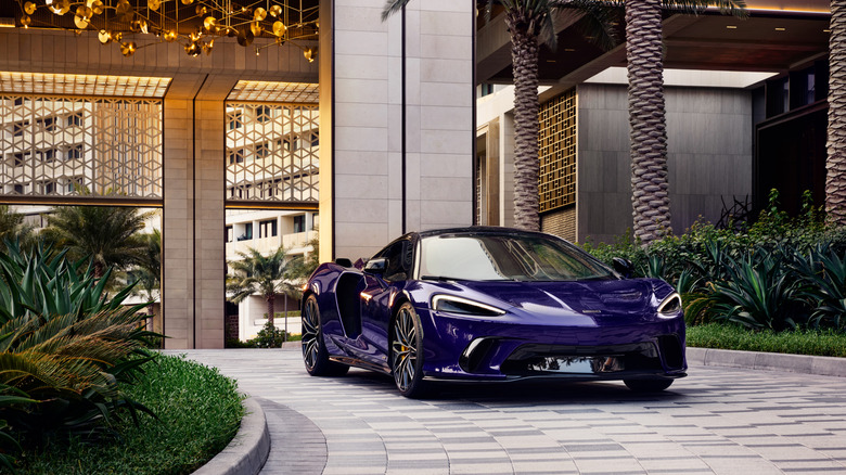 A purple McLaren GTS parked in front of a luxury hotel.