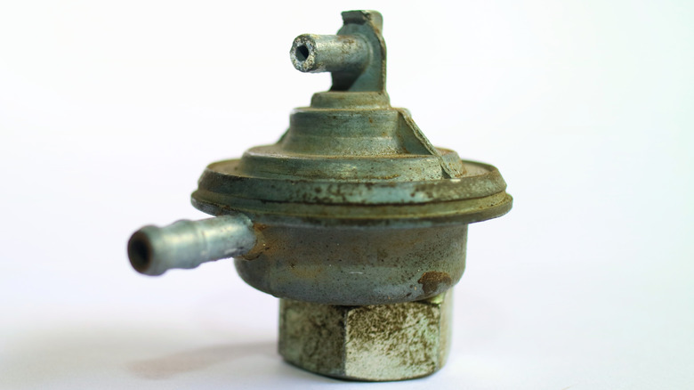 The weathered diaphragm unit of a mechanical fuel pump against an off-white background.
