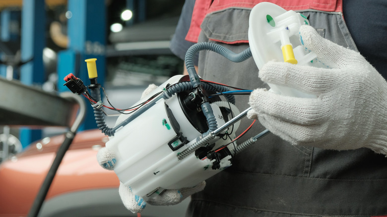 A gloved technician holding an in-tank electric fuel pump.