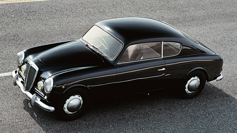 A black Lancia Aurelia GT B20 coupe against a road backdrop