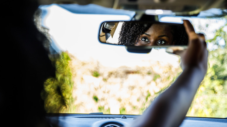 Young black woman looks into rearview mirror of her car.