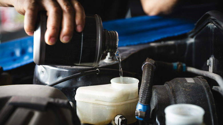 Close up on mechanic's hand adding brake fluid under a car's hood