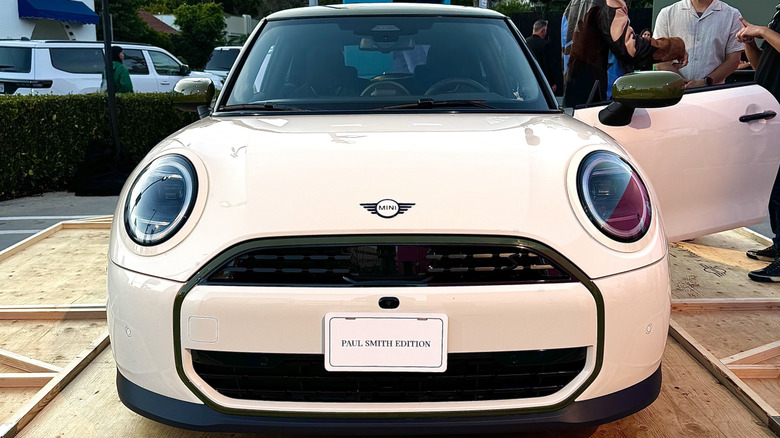 A close-up head-on shot of an Inspired White Mini Cooper S Two-Door parked on plywood with the driver's door open