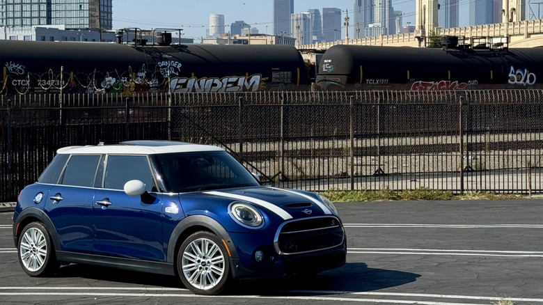 A front three-quarters shot of my blue Mini Cooper S four-door with white stripes and a white roof parked in a lot next to a train in front of the LA Skyline