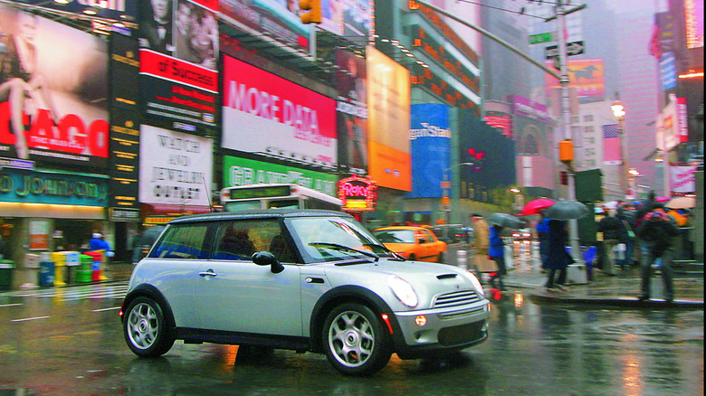 A side shot of a silver first-gen Cooper S driving around a corner on a rainy day in New York City