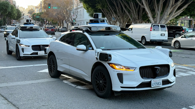 Front 3/4 view of two Waymo robotaxis turning right at an intersection in the city