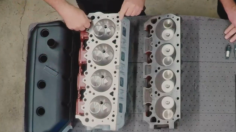 A Chrysler Hemi head and black valve cover next to a wedge head on a workbench, showing the differences in combustion chamber design