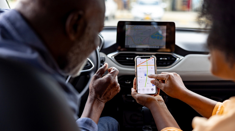 Two people inside a car going over their intended route on a navigation app before embarking
