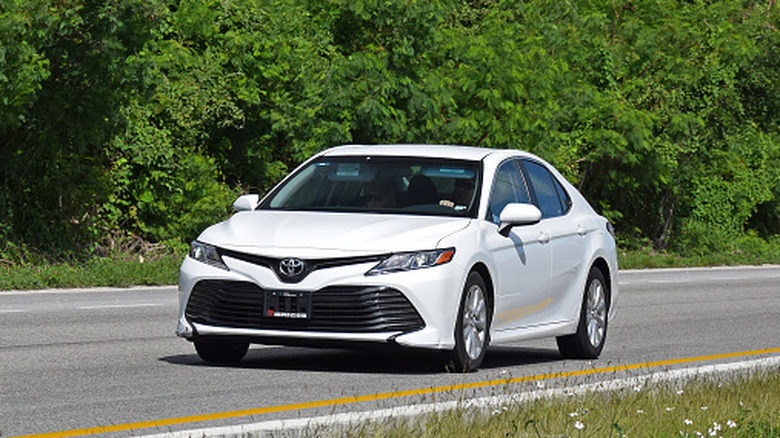 A white Toyota Camry drives on the road