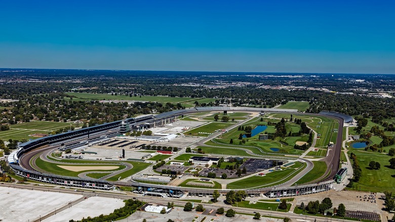 An aeiral view of the Indianapolis Motor Speedway on a clear day with flat Indiana landscape stretching away behind it