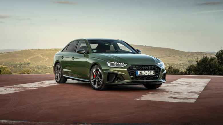 A green Audi A4 sits on a helicopter pad with hills in the background