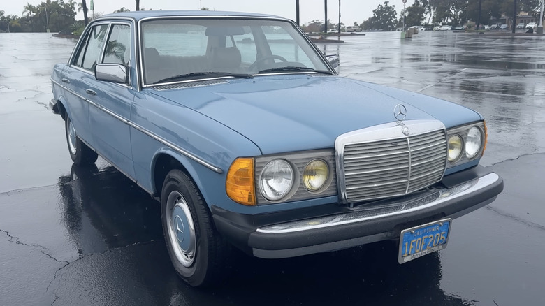 A blue Mercedes-Benz W123 300D sits in a wet parking lot.
