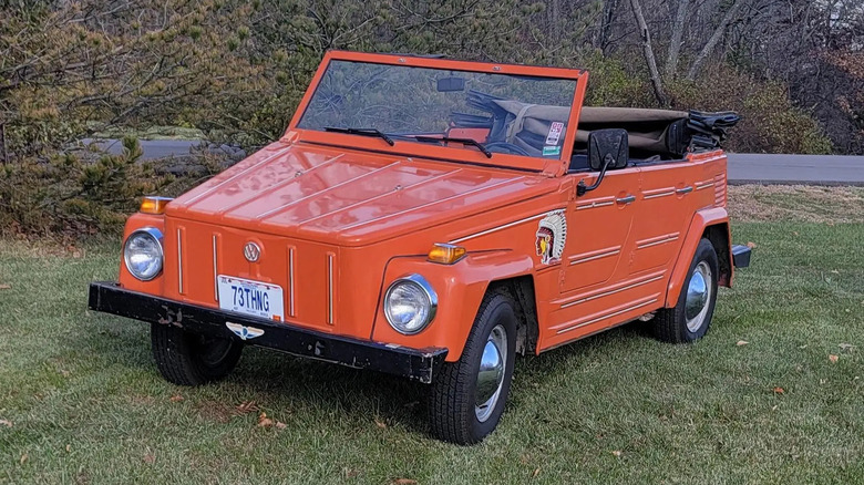 Front three quarters shot of an orange VW Thing with its roof down parked on grass