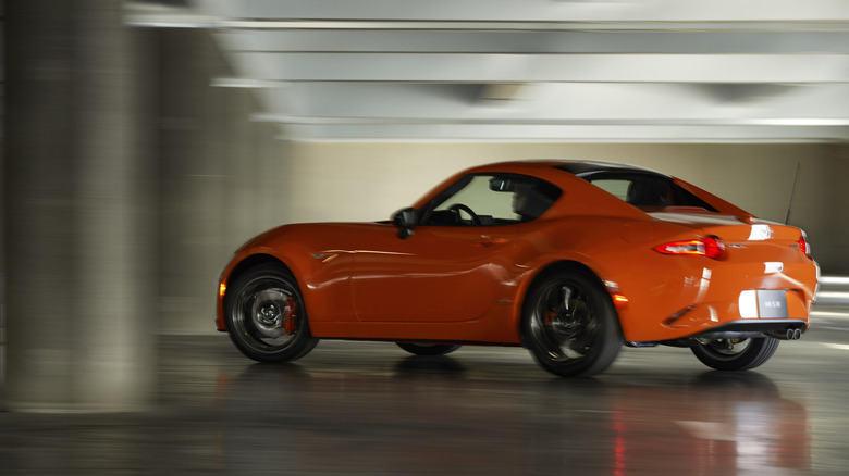 a rear three quarters shot of an orange MX-5 RF driving in a parking structure