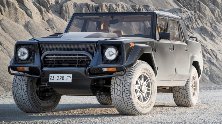 A dusty black Lamborghini LM002 SUV parked on a dirt road next to a rocky vista