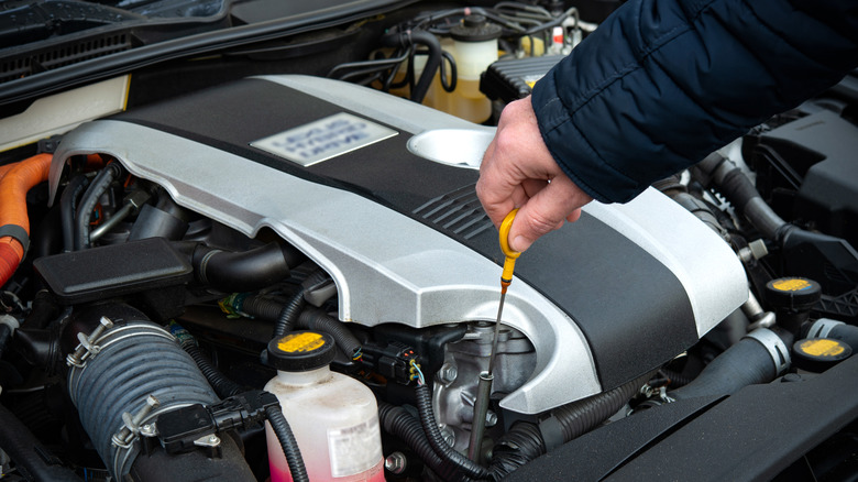 A person pulling the dipstick to check the oil of a car engine