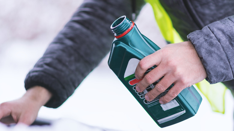 A person pouring fresh oil into an engine during snowy weather