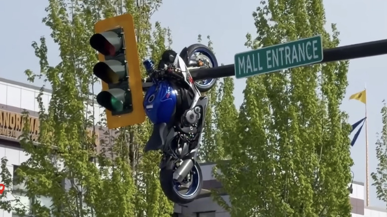A motorcycle hangs by its front fork from a traffic light pole after a crash