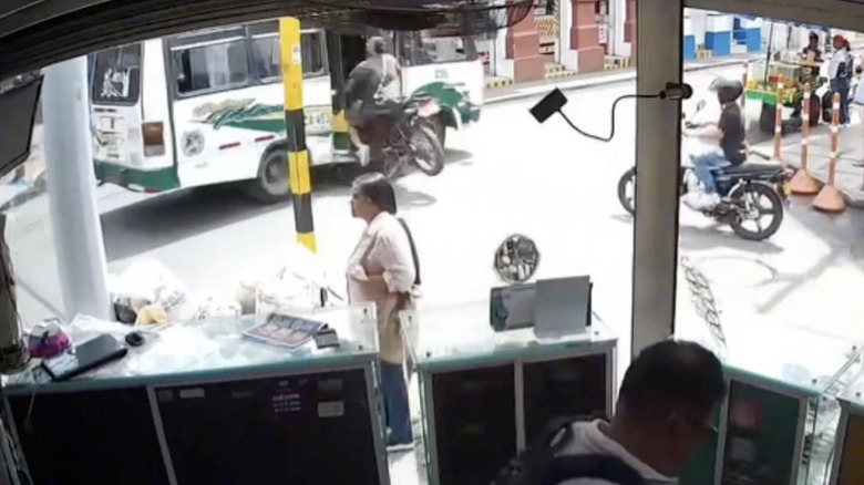 Security camera view showing a motorcycle crashing into the open side door of a bus in an intersection