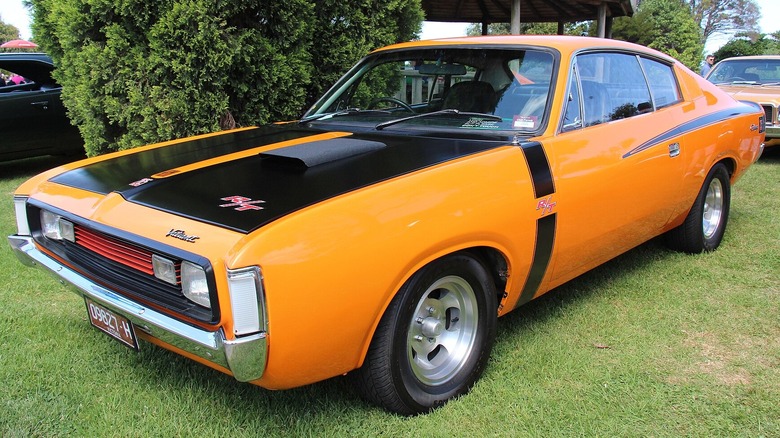 A bright orange 1972 Chrysler Valiant VH Charger R/T coupe parked on a grassy patch.